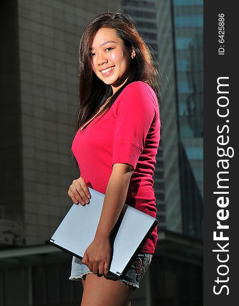 Picture of an Asian Girl carrying a notebook with office landscape behind. Suitable for contexts of office environment, casual staff, part-timers, and even interns. Picture of an Asian Girl carrying a notebook with office landscape behind. Suitable for contexts of office environment, casual staff, part-timers, and even interns.