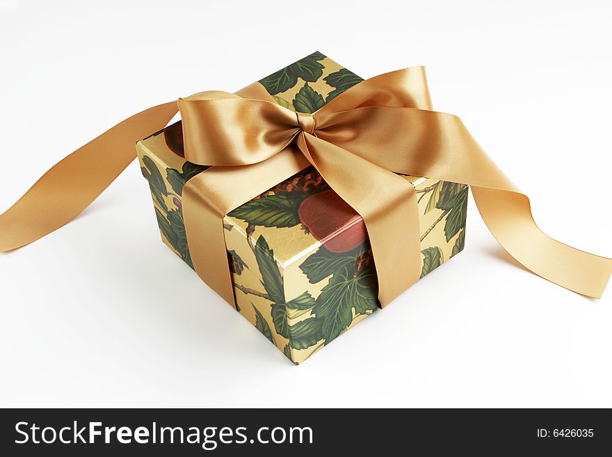 Gift box in autumn or winter colors tied with soft gold satin ribbon on white background