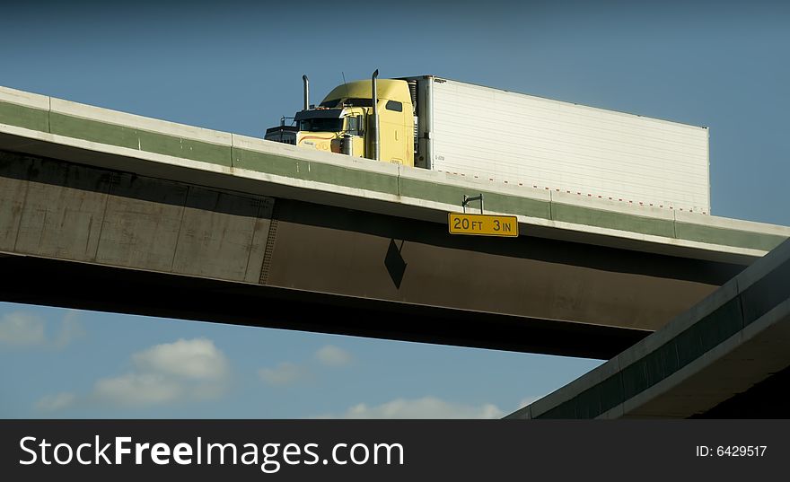 A yellow eighteen wheeler driving on an overpass.