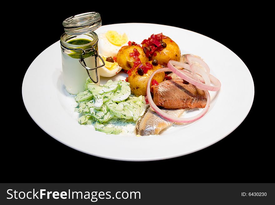 Herring with boiled potatos and cucumber salad on a white plate isolated on black