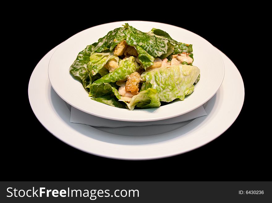 Caesar salad with shrimps on a white plate isolated on black