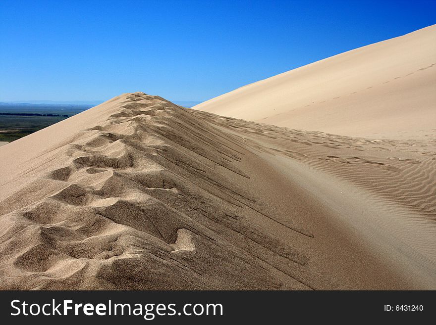 Trail of footprints on top of ridge of sand dune formation against blue sky. Trail of footprints on top of ridge of sand dune formation against blue sky