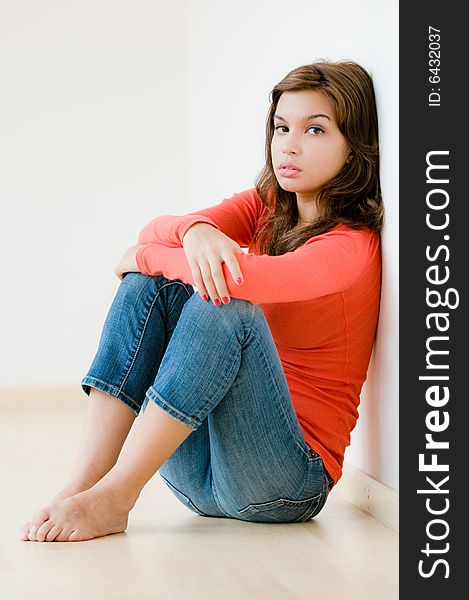 A lifestyle shot of a young woman sitting down on the floor of her modern home