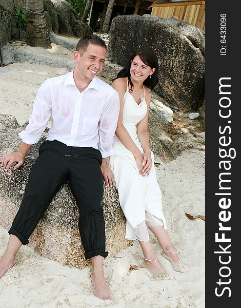 Bride and groom sitting on a rock at the beach.