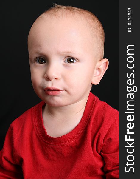 Blonde toddler against a black background with a serious expression