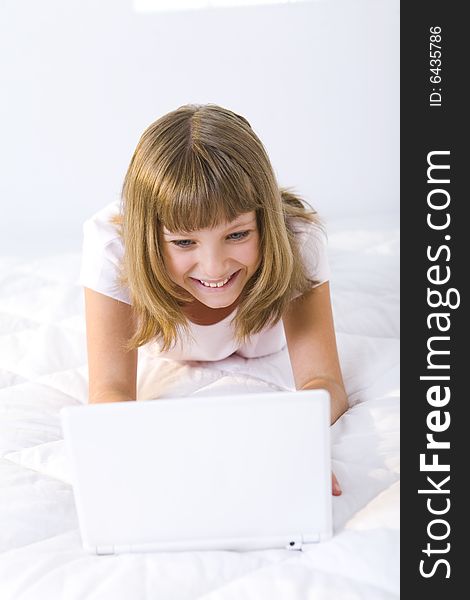 Young smiling girl lying on a bed and does something on laptop. Young smiling girl lying on a bed and does something on laptop.