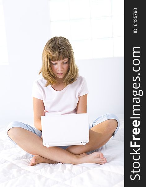 Young girl sitting cross-legged on a bed and does something on laptop. Young girl sitting cross-legged on a bed and does something on laptop.