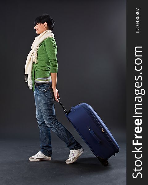 The young girl in a scarf and jeans with a dark blue suitcase on a dark background