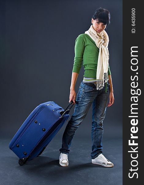 The young girl in a scarf and jeans with a dark blue suitcase on a dark background