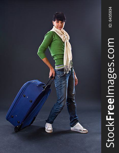 The young girl in a scarf and jeans with a dark blue suitcase on a dark background