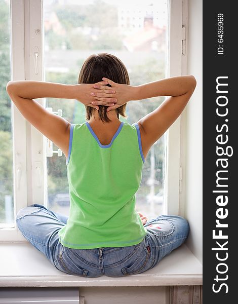 Young girl in green t-shirt is sitting on window-sill. Young girl in green t-shirt is sitting on window-sill