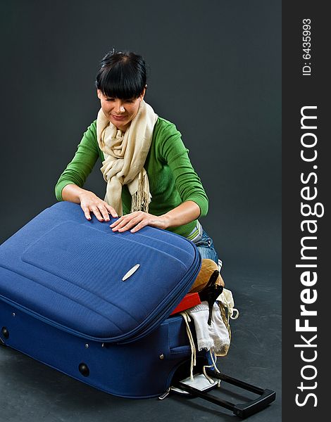 The young girl in a scarf and jeans with a dark blue suitcase on a dark background