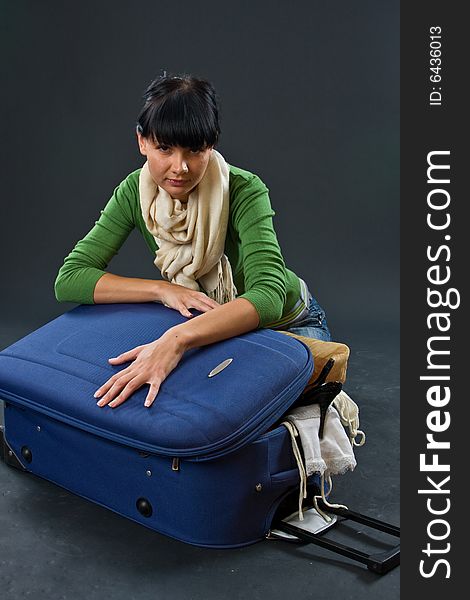 The young girl in a scarf and jeans with a dark blue suitcase on a dark background