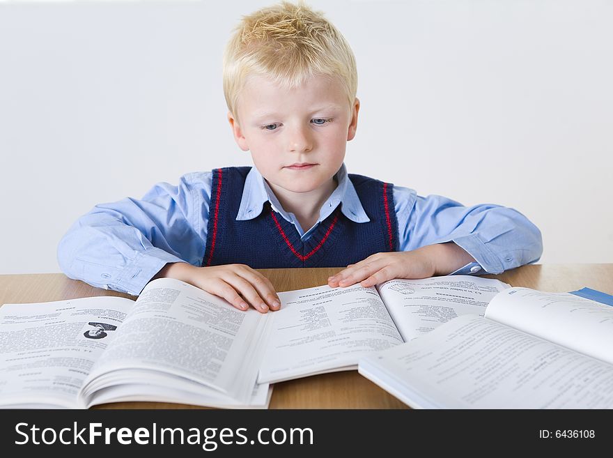 Young boy sitting at desk and reading books. Front view. Young boy sitting at desk and reading books. Front view.
