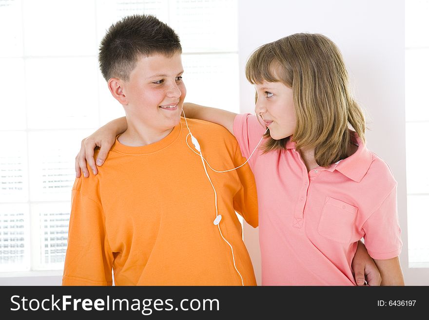 Boy and girl standing in front of window and listening to music by earphones. They smiling and looking each other. Boy and girl standing in front of window and listening to music by earphones. They smiling and looking each other.