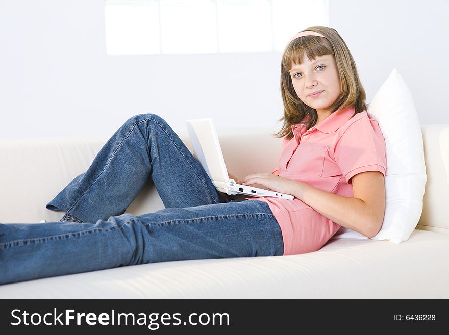 Young girl with laptop sitting on couch. She's smiling and looking at camera. Young girl with laptop sitting on couch. She's smiling and looking at camera.