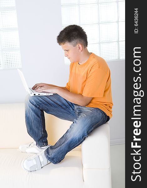 Young boy sitting on couch and typing on laptop. Young boy sitting on couch and typing on laptop.