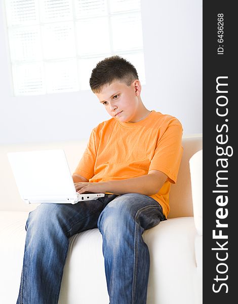 Young boy with laptop sitting on couch. He looks unhappy.