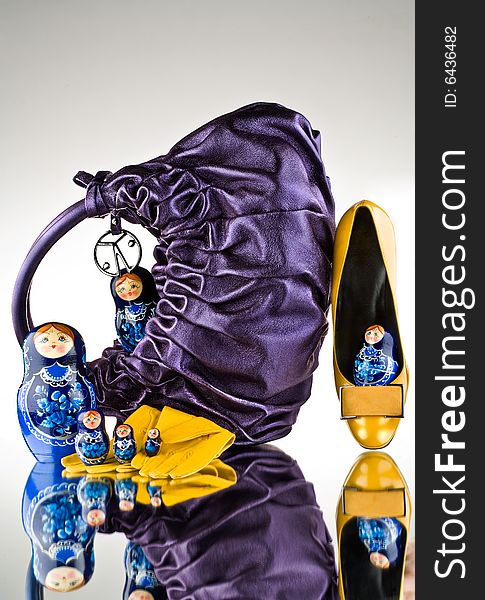 A purple handbag on a glass surface with yellow gloves and shoes next to Russian Babushka nesting dolls. A purple handbag on a glass surface with yellow gloves and shoes next to Russian Babushka nesting dolls.