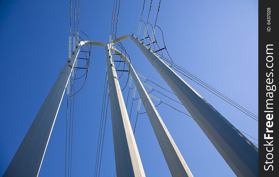 White power pole tower with lots of power lines from its base to the blue sky