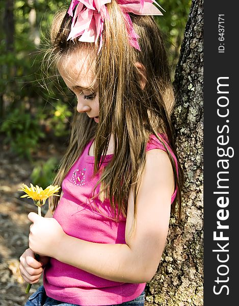 Little girl admiring her yellow flower while leaning against a tree. Little girl admiring her yellow flower while leaning against a tree.