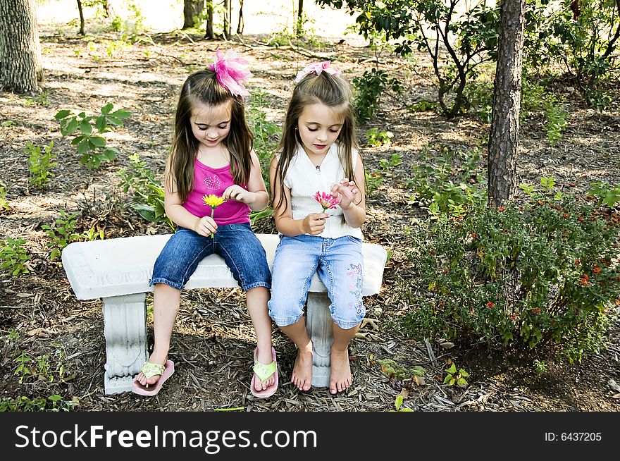 Two little girls pulling pedals from their flowers saying he loves me, he loves me not.