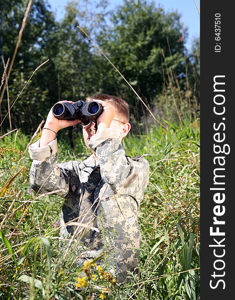 Young boy in field, in camofllage, looking up through binoculars. Young boy in field, in camofllage, looking up through binoculars