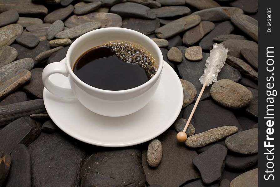 Cup of coffee against black stones and reed sugar