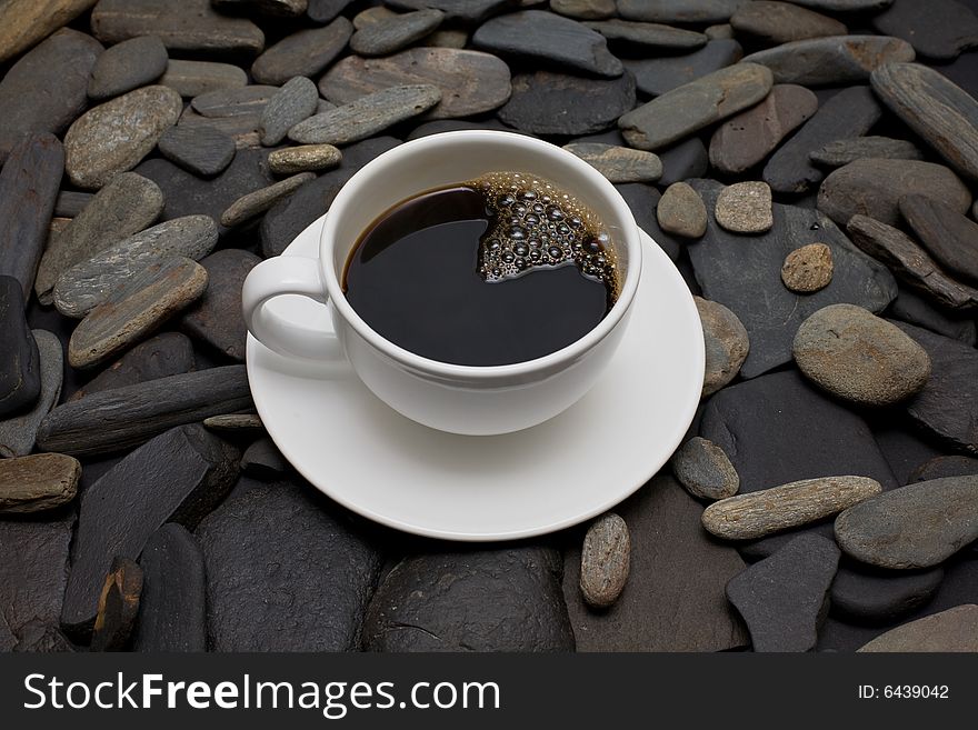 White cup of coffee against black stones