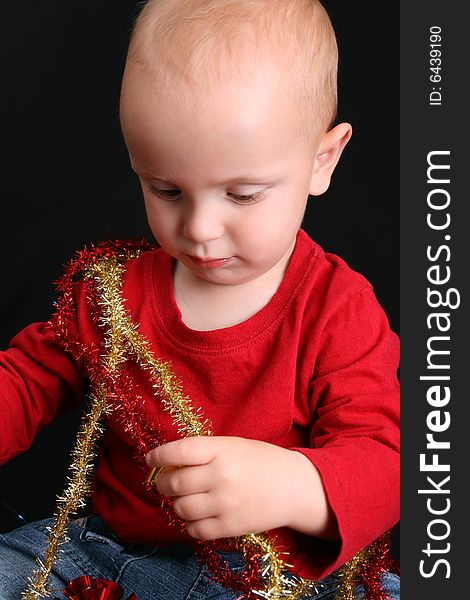 Toddler against a black background playing with Christmas decorations