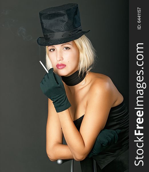 Young blonde woman in black hat keeps a cigarette and looks ahead. Young blonde woman in black hat keeps a cigarette and looks ahead.