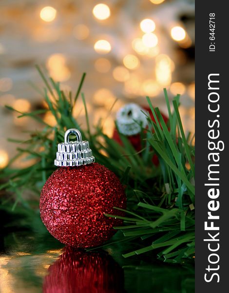 A red Christmas ornament with a slight soft focus and blurred Christmas lights in the background.