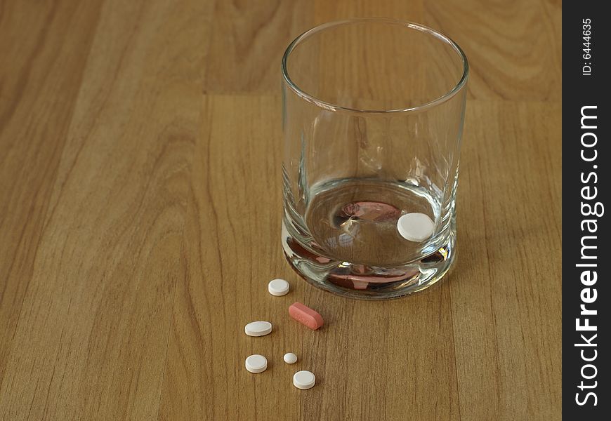 A GLass with a dissolving tablet on the inside and some pills beside it. A GLass with a dissolving tablet on the inside and some pills beside it