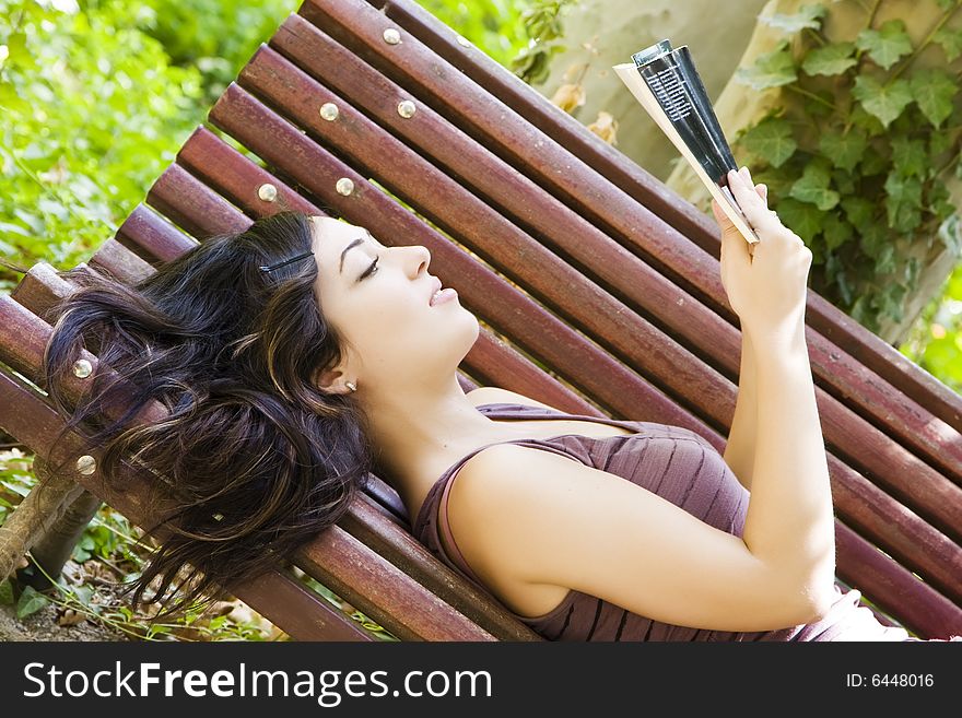 Reading woman laying in a park bench. Reading woman laying in a park bench.