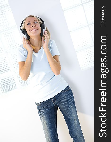 Young smiling woman listening to music by headphones. She's looking up. Front view. Young smiling woman listening to music by headphones. She's looking up. Front view.