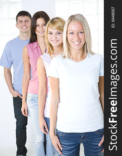 Group of friends standing in the line. They're smilling and looking at camera. Focused on second girl. Front view. Group of friends standing in the line. They're smilling and looking at camera. Focused on second girl. Front view.