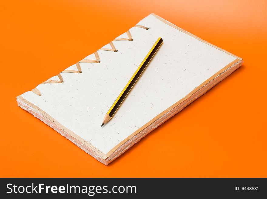 Recycled notepad and pencil over an orange background