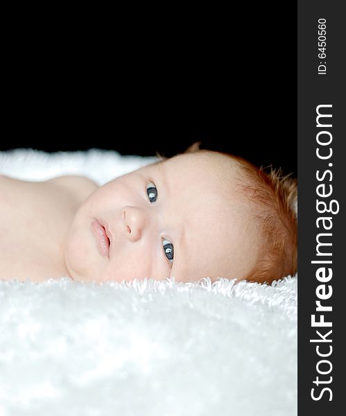 A young baby is laying down in a studio.  He is looking away from the camera.  Vertically framed shot. A young baby is laying down in a studio.  He is looking away from the camera.  Vertically framed shot.