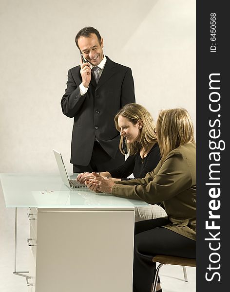 Three people are together in a room at a table. They are all looking at each other and the man is standing up and talking on a cell phone. It appears to be a business meeting and there is a laptop on the table in front of the youngest member. Vertically framed shot. Three people are together in a room at a table. They are all looking at each other and the man is standing up and talking on a cell phone. It appears to be a business meeting and there is a laptop on the table in front of the youngest member. Vertically framed shot.