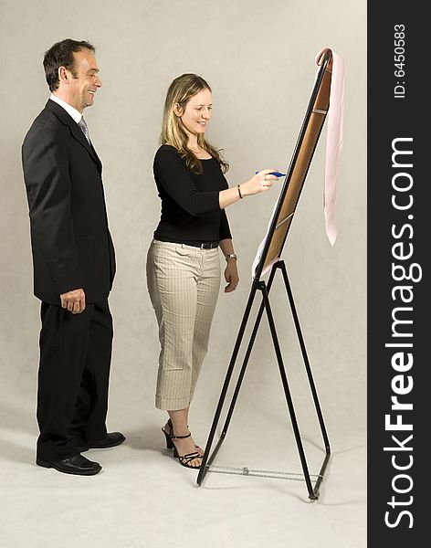 A man is standing next to a young woman who is drawing on a large board.  It looks as if she is drawing a business model.  They are smiling and looking at the board.  Vertically framed shot. A man is standing next to a young woman who is drawing on a large board.  It looks as if she is drawing a business model.  They are smiling and looking at the board.  Vertically framed shot.