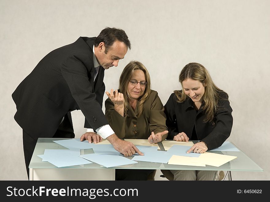 Two women and a man in a meeting at a desk with talking over paperwork. Horizontally framed photo. Two women and a man in a meeting at a desk with talking over paperwork. Horizontally framed photo.