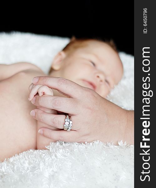 A baby is laying down in a studio. A mother is holding the baby's hand. Vertically framed shot. A baby is laying down in a studio. A mother is holding the baby's hand. Vertically framed shot.