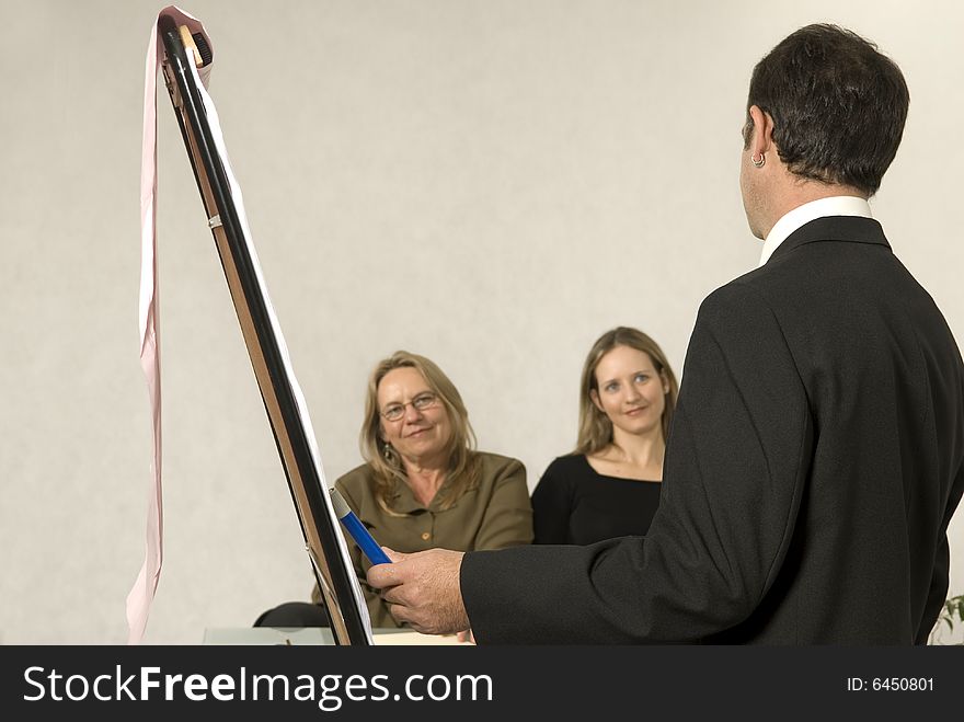 A Boss in instructing his employees in a business meeting. The two girls are smiling at him. Horizontally framed shot. A Boss in instructing his employees in a business meeting. The two girls are smiling at him. Horizontally framed shot.