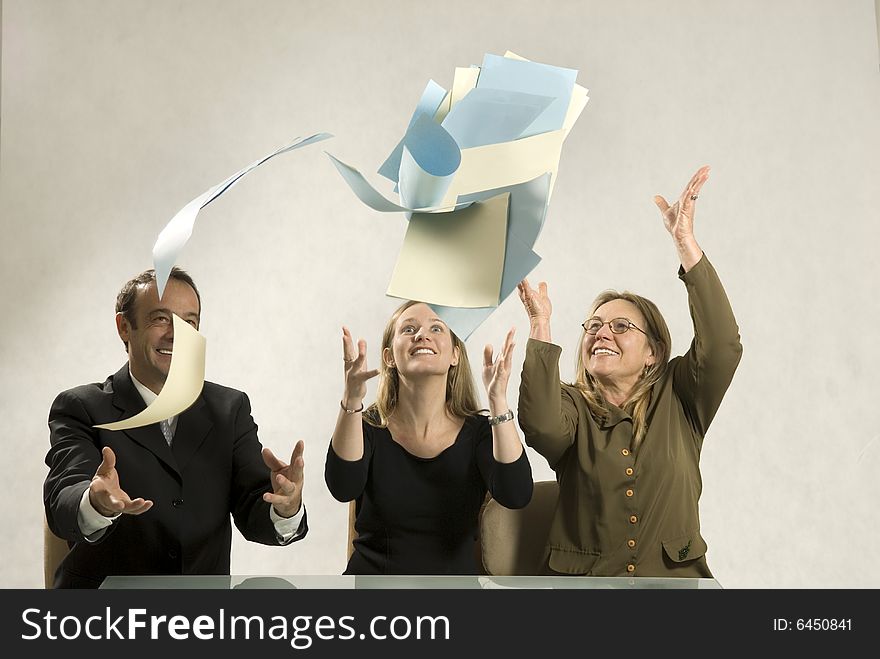 Three colleagues smiling and throwing their papers in the air. Horizontally framed photo. Three colleagues smiling and throwing their papers in the air. Horizontally framed photo.