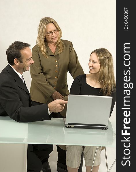 Two women and a man in a meeting at a desk with a laptop. They are all smiling. Vertically framed photo. Two women and a man in a meeting at a desk with a laptop. They are all smiling. Vertically framed photo.