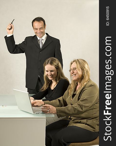 Three people are together in a room at a table. They are all looking at each other and the man is standing up and holding out a cell phone. It appears to be a business meeting and there is a laptop on the table in front of the older woman. Vertically framed shot. Three people are together in a room at a table. They are all looking at each other and the man is standing up and holding out a cell phone. It appears to be a business meeting and there is a laptop on the table in front of the older woman. Vertically framed shot.