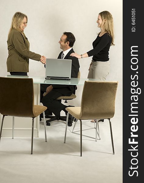 Three colleagues in a meeting. A woman is giving a man a shoulder rub as he sits facing another woman an shakes her hand. Vertically framed photo. Three colleagues in a meeting. A woman is giving a man a shoulder rub as he sits facing another woman an shakes her hand. Vertically framed photo.