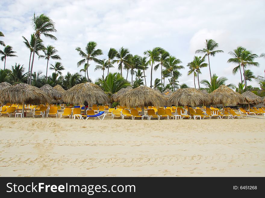 Empty loungers on a tropical beach with palm trees in Punta Cana, Dominican Republic. Empty loungers on a tropical beach with palm trees in Punta Cana, Dominican Republic