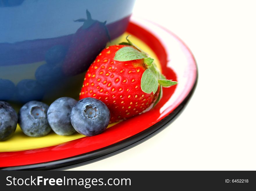 Blueberries and a strawberry on a color coordinated plate with a bowl all isolated on a white background. Blueberries and a strawberry on a color coordinated plate with a bowl all isolated on a white background