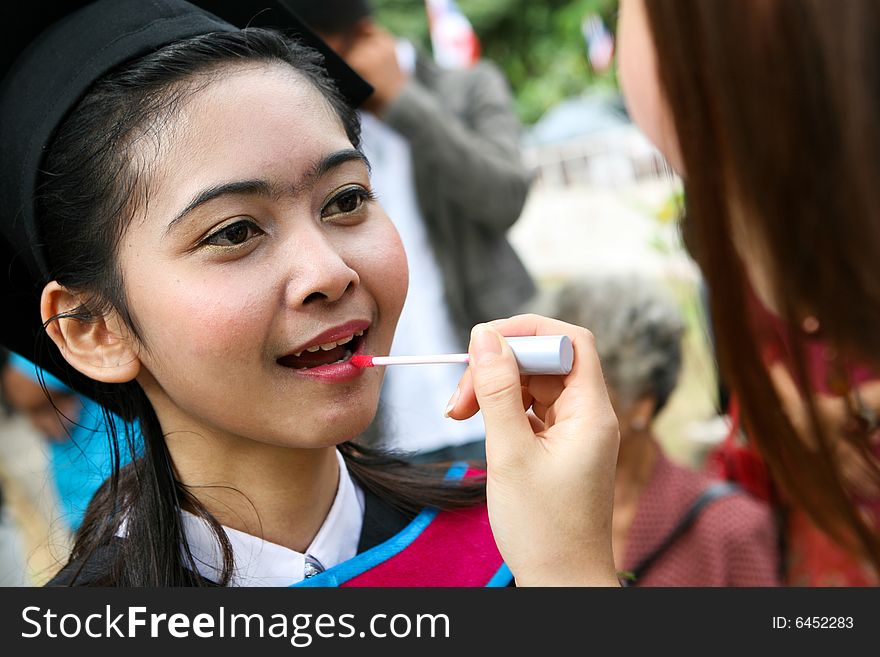 Asian university graduate having her lipstick applied by a make-up artist.